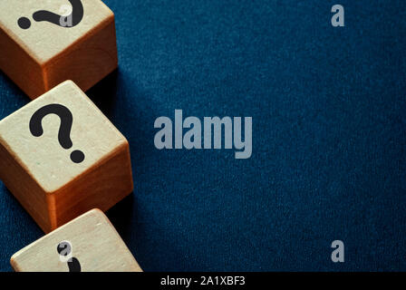 Bordo laterale dei punti interrogativi su cubi di legno su un blu scuro dello sfondo testurizzata con spazio di copia Foto Stock