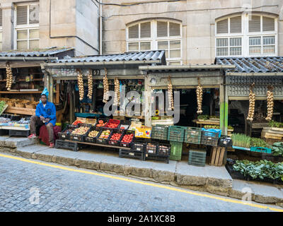 Un negozio uomo sul mercato di Ourense città presso il suo stand pieno di verdure fresche Foto Stock