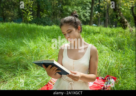 Ragazza giace su un plaid sull'erba e legge un libro Foto Stock