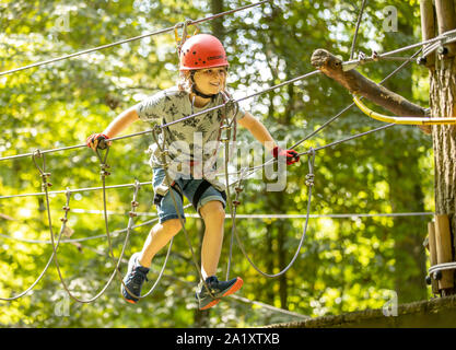 Falesia, corso di arrampicata, boy, 9 anni, con il casco e il cablaggio a un corso di arrampicata in una foresta, Foto Stock