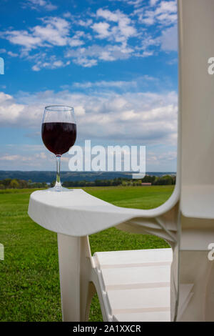 Un bicchiere di vino rosso fotografati a sul bracciolo di un bianco di plastica sedia Adirondack vicino lago Cayuga nella regione dei Laghi Finger dello Stato di New York Foto Stock