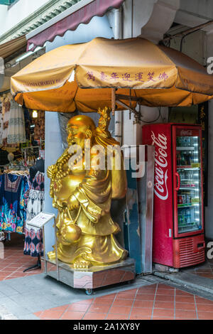 Singapore - Marzo 22, 2019: Chinatown. Golden laughting statua del Buddha utilizzato da Venhonia carità per raccogliere fondi nella parte anteriore del negozio di sago Street. Rosso C Foto Stock