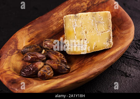 Pezzo di vecchio formaggio blu ed un ramo di date giacciono su di un piatto di legno. Vista da sopra Foto Stock