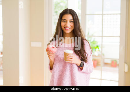 Giovane lavoratore donna prendendo una pausa mangiando una gustosa ciambella rosa e bere una tazza di caffè Foto Stock