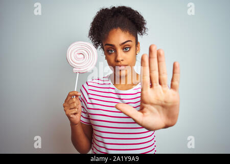 African American teenager donna mangiando caramelle colorate isolato su sfondo bianco con mano aperta facendo segno di stop con gravi e fiducioso express Foto Stock