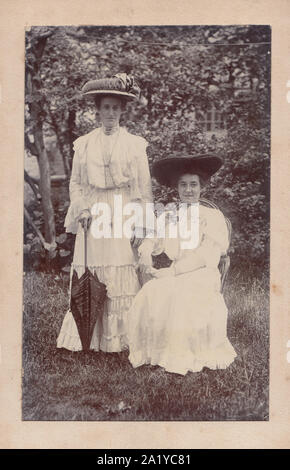 Armadio vittoriano Card che mostra due donne alla moda in posa di un giardino. Entrambe belle da indossare cappelli. La signora permanente tenendo un ombrello. Foto Stock