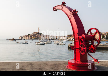 Ampio angolo di immagine di una vecchia barca rossa con gru come si inizia ad arco la graziosa città vecchia di Rovigno in background.