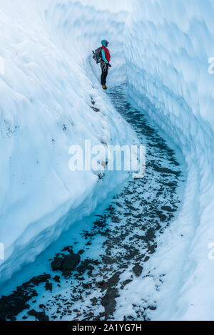 Una giovane donna di guidare i clienti di tutto il ghiacciaio Matanuska si ferma in un canyon tagliato dal ghiaccio in attesa sui suoi clienti. Indossa un cablaggio, zaino un Foto Stock