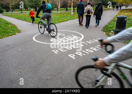I ciclisti a cavallo su un pedone priorità segno di avvertimento su un percorso di parco in parco di Victoria, Tower Hamlets, Londra Foto Stock