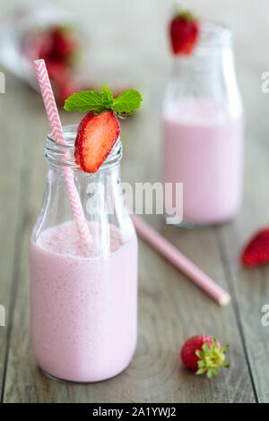 Un sano frullato fragole, milk shake, in bottiglie tradizionali con fragole sparse e rosa paglia sopra uno sfondo di legno. Composi verticale Foto Stock