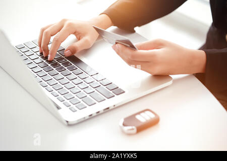 Donna mani utilizzare computer laptop, carta di credito e la chiave auto per pagamento mensile Foto Stock