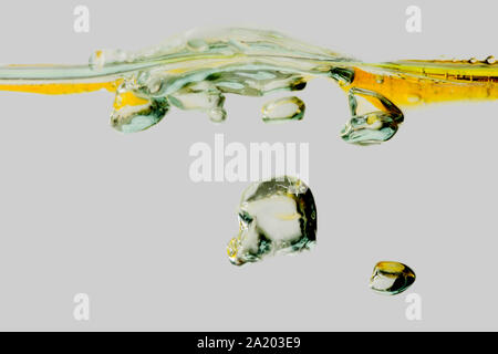 Vista laterale di un increspata superficie di acqua miscelata con olio vegetale e le bolle in isolati contro uno sfondo bianco. Foto Stock
