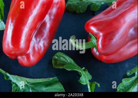 Res peperoni e foglie di rucola su un nero sfondo rustico Foto Stock