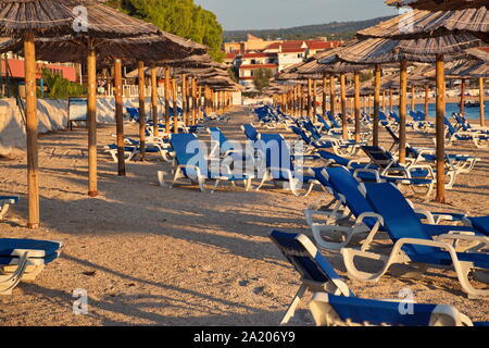 Gruppo di ombrelloni e sedie a sdraio sulla spiaggia di Primosten in sunset Foto Stock