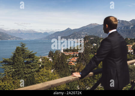 L'uomo guarda sul lago di Como vista montagna. Bellagio città vista aerea. Il lusso e la ricca vita concetto. Conseguimento di successo. Foto Stock