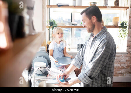 Figlia sorridente e parlando di daddy lavando i piatti Foto Stock