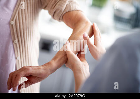 Disponibile infermiere mettendo la crema sul raccordo a gomito per pensionati donna Foto Stock