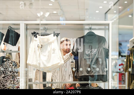 Bel giovane scegliendo abiti alla moda nella boutique di moda nel centro commerciale della città Foto Stock