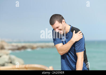 Doloroso runner lamenta sofferenza spalla ache dopo lo sport sulla spiaggia Foto Stock