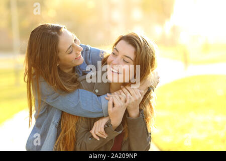 Due amici Allegro scherzando piggybacking riuniti in un parco al tramonto Foto Stock