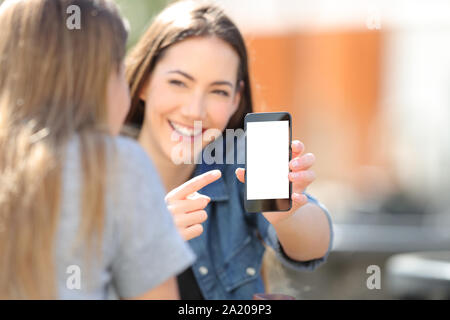 Felice ragazza mostra blak smart phone schermo per il suo amico in strada Foto Stock