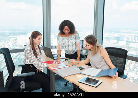 Femmina i responsabili marketing puntando al grafico con le statistiche finanziarie sulla scrivania e discutere le nuove tendenze nel settore vendite Foto Stock