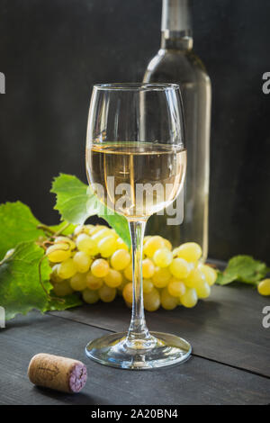 Bottiglia di vino bianco con wineglass, uva matura sui tavoli in legno nero. Close up. Foto Stock