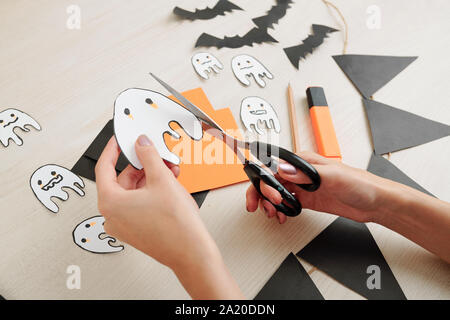 Le mani della donna il taglio di simpatici fantasmi al di fuori della carta per la festa di Halloween Foto Stock