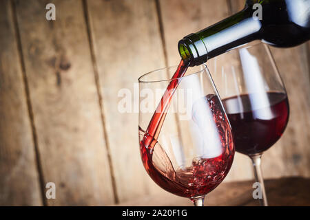 Un bicchiere di vino rosso secco versata da una bottiglia in elegante wineglasses su legno rustico con spazio di copia Foto Stock