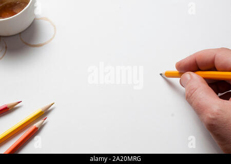 Man tenere una matita su un foglio bianco di carta, matite, caffè cup e macchie di caffè come decorazione, vista dall'alto Foto Stock