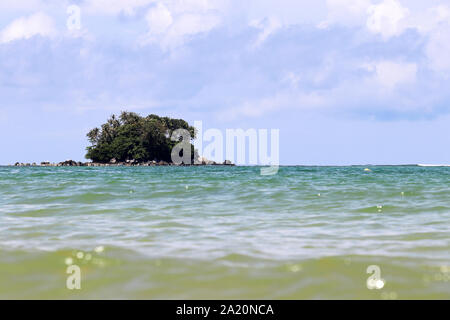 Isola tropicale con palme in un oceano, pittoresca vista dall'acqua calma, il fuoco selettivo. Seascape colorato con cielo blu e nuvole bianche Foto Stock