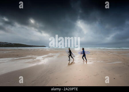 Surfers camminando sul Fistral Beach come buio fosche nubi approccio in Newquay in Cornovaglia. Foto Stock