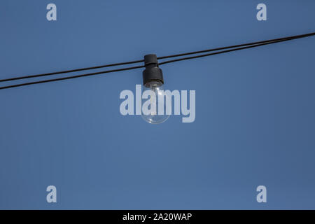 Vista di una vecchia lampada ad incandescenza, cablata al di fuori sulla strada con il cielo azzurro sfondo... Foto Stock