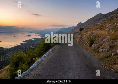 Una stretta e tortuosa strada che corre sul bordo di una scogliera sopra il Lago di Scutari in Montenegro Foto Stock