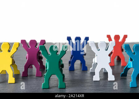 Colorate diverse persone in miniatura statuette in piedi in fila su una pietra scura piastra di ardesia. Isolato su sfondo bianco. La diversità concetto astratto. Foto Stock