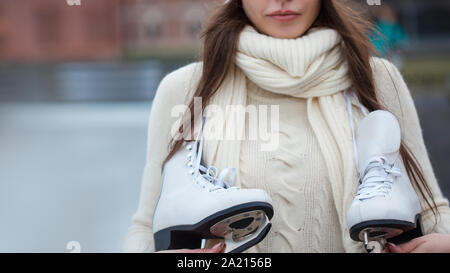 Affascinante giovane donna nel parco vicino alla pista di pattinaggio sul ghiaccio. Sorridente brunette con pattini. Close-up, copia spazio sulla sinistra. Foto Stock