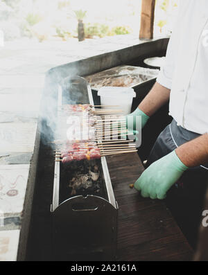 L'uomo la cottura del cibo di strada molti spiedini con carne di agnello cotta alla brace, chiamato arrosticini in Italia. Foto Stock