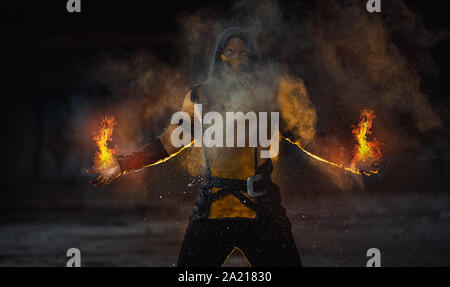 L'uomo raffigurante un guerriero Scorpion con fiamma dalle sue mani pone al background di fumo. Foto Stock