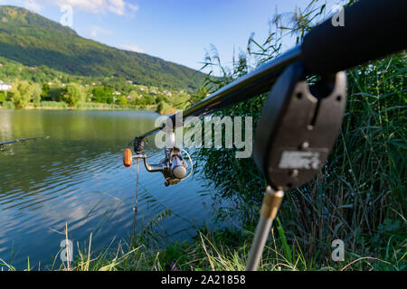 Primo piano di una bobina in canna da pesca su un puntello in background di un lago e montagne. Foto Stock