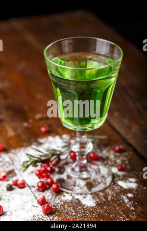 Cocktail verde sulla base di assenzio in un elegante vintage vetro su di un legno marrone. sfondo dello zucchero bianco e mirtilli sono sparsi nei dintorni Foto Stock