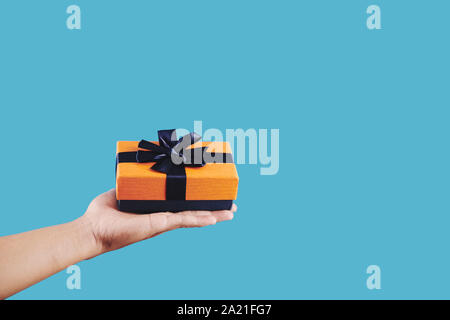 Mano con presente avvolto in blu e arancione carta con grande arco Foto Stock