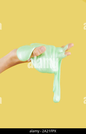 Il gocciolamento melma verde in mano della persona contro sfondo giallo Foto Stock