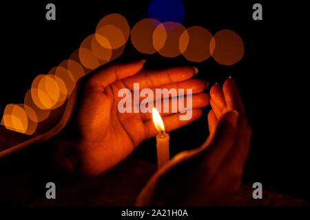 Mani che proteggono la fiamma di una candela al buio durante il Diwali celebrazione festosa notte con bokeh in background. Concetto di tradizione religiosa Foto Stock