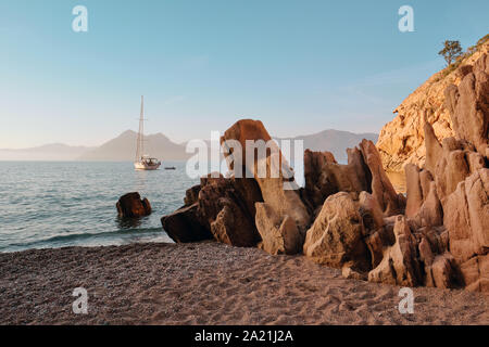 Uno yacht, granito rosso formazioni rocciose e spiaggia di Plage de Ficaghjola / Plage de Ficajola e il golfo di Porto, Calanques de Piana Corsica Francia. Foto Stock