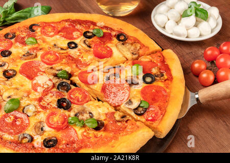 Salsiccia per pizza pizza con fette di salame, olive nere, funghi, di foglie di basilico fresco e un sacco di formaggio, al buio su un rustico sfondo di legno Foto Stock