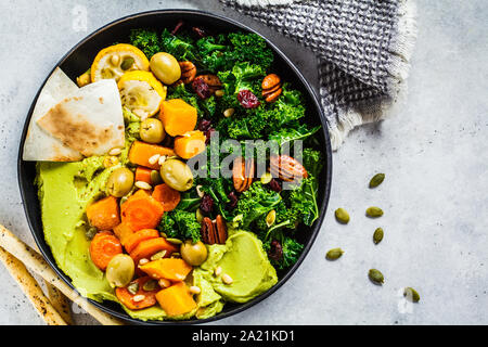 Avocado hummus con verdure al forno, olive, noci e bacche in una piastra nera. Sano cibo vegan concetto. Foto Stock