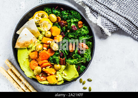 Avocado hummus con verdure al forno, olive, noci e bacche in una piastra nera. Sano cibo vegan concetto. Foto Stock