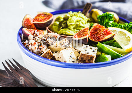 Ciotola di Buddha con la quinoa, tofu, kale, fichi e guacamole hummus in una piastra bianca. Foto Stock