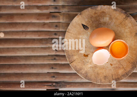Uova di colore marrone su un tagliere di legno vi è un tuorlo nel guscio dell'uovo. L'uovo marrone ha una goccia di acqua perché è la rimozione dal frigorifero Foto Stock