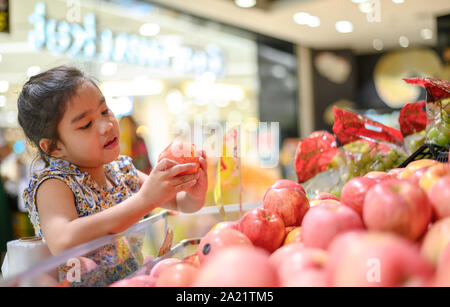 Asian bambina scegliendo un Apple in un negozio di alimentari o supermarket Foto Stock